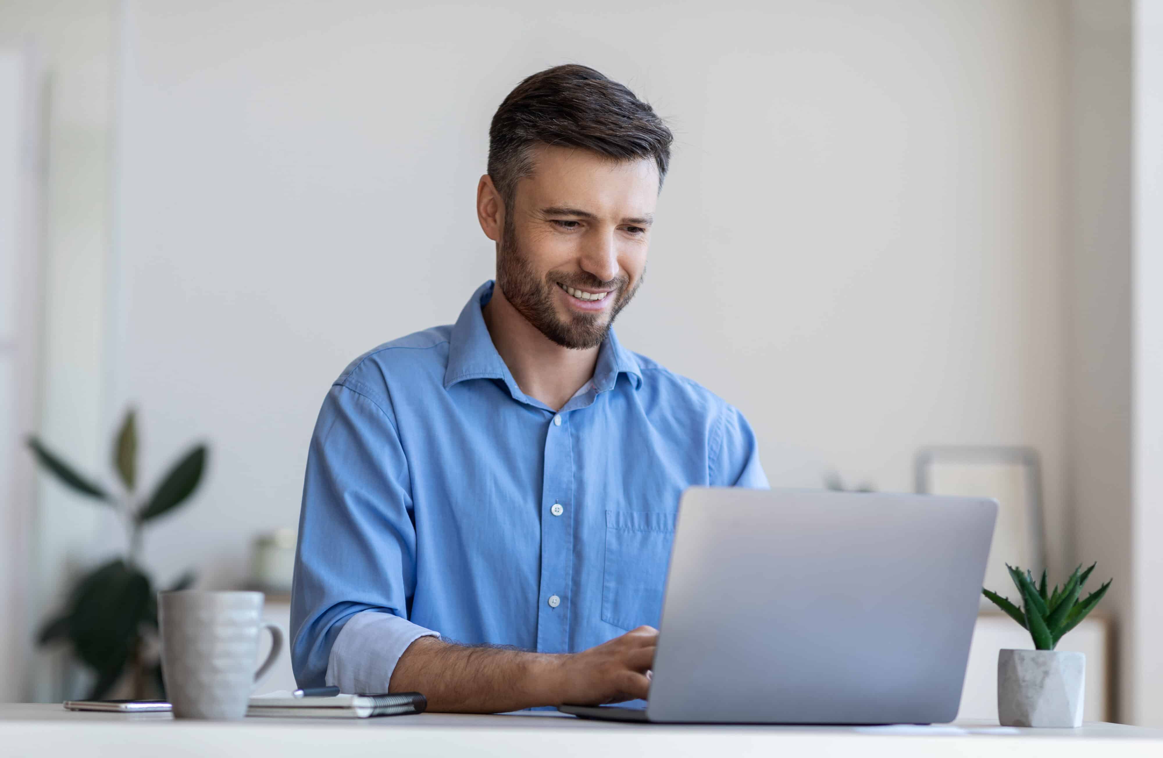 Handsome male entrepreneur working on laptop at desk in modern office